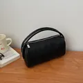 Minimalist black lychee texture cylinder handbag with silver zipper on wooden table - Black