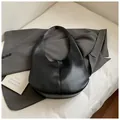 Minimalistische schwarze Hobo-Tasche mit Leder-Lychee-Struktur auf einem grauen Sakko - Schwarz