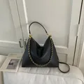 Black lychee texture hobo bag with gold woven chain strap on a white sofa - Black