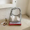 Close-up of metallic silver pleated handbag with ruched handle on decorative books - Silver