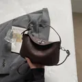 Dunkelbraune minimalistische Handtasche aus Leder mit Silberverschluss auf grauem Sakko - Braun