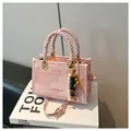 Bolso bandolera rosa con asas trenzadas y colgante de cuentas sobre libros blancos - Rosa