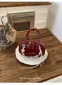 Detail der weinroten Mini-Lederhandtasche mit Kontrastnähten und Perlen-Anhänger - Rot