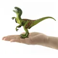 Detailed close-up of a miniature green Velociraptor dinosaur model held in a palm - Green Spotted Style / Green