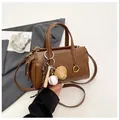 Bolso Boston marrón en ecopiel con un colgante de béisbol y detalles dorados - Café con colgante