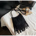 Flat lay of black fringe shoulder bag with bohemian tassels and long straps on a bed - Black