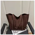 Détail du grand sac cabas en daim marron avec rivets argentés posé sur une chaise - Café