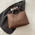 Dunkelbraune große Shopper-Tasche mit Ziernähten auf grauem Blazer-Hintergrund - Braun