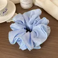Light blue oversized scrunchie with pleated texture and pearl luster on a wooden desk - Blue
