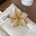 Elegant cream yellow frangipani hair claw with gold metal edges on woven background - Khaki