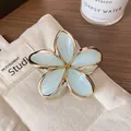 Goldene Frangipani-Blütenhaarklammer mit hellblauen Blütenblättern auf beigem Stoff - Hellblau