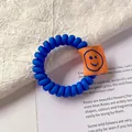 Blue spiral phone line hair tie with orange smiley face tag in minimalist style - Sapphire Blue