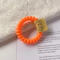 Orange spiral hair tie with smiley face tag accessory on creative artistic background - Orange