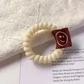Creamy spiral telephone wire hair tie featuring a cute brown smiley face fabric label - Cream