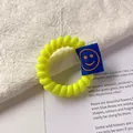 Elastico per capelli a spirale giallo neon con etichetta smiley blu su sfondo chiaro - giallo fluorescente
