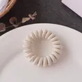 Beige spiral hair tie with ribbed fabric texture on a white ceramic plate - Off White