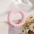 Pink matte spiral telephone cord hair tie on aesthetic white fabric background - Pink
