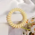 Simple matte pale yellow spiral telephone wire hair tie on a white fabric background - Neon Yellow