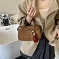 Detail of vintage brown suede handbag with decorative pompom charm and leather strap buckle - With Pendant / Brown