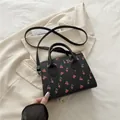 Stylish black handbag with red cherry print featuring top handles and long strap - Black