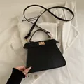 Bolso de hombro trapezoidal negro minimalista con cierre dorado sobre tela blanca - Negro