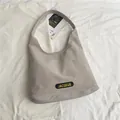 Sac fourre-tout gris minimaliste en nylon avec étiquette JACQEUE sur un décor plat - Blanc Cassé