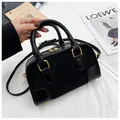 Sac Boston noir avec détails dorés et bandoulière chaîne sur fond de tissu blanc - Noir