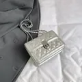 Silver quilted crossbody bag with metallic chain strap and turn-lock closure on grey suit - Silver