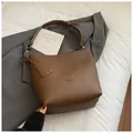 Détail du sac seau HOCOMU en cuir marron avec texture litchi et logo sur un costume d'affaires - Marron