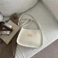 Minimalistische cremeweiße Leder-Achseltasche mit Goldplatte auf dem Sofa - Weiß