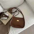 Vintage braune Unterachseltasche aus Leder mit Goldlogo auf weißem Sofa-Set - Braun