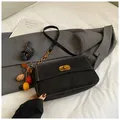 Matte black crossbody handbag with gold clasp and decorative pendant on grey blazer - Black With Pendant