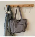 Graue große Tragetasche mit mehreren Taschen an einem hölzernen Wandregal hängend - Grau