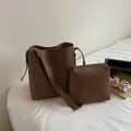 Detalle de conjunto de bolsos tipo cubo en cuero marrón con neceser y portátil en mesa - Estilo Bolso Cubo Y Neceser / Caqui