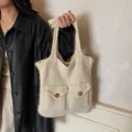 Cremefarbene Stricktasche mit zwei Fronttaschen und braunen Knöpfen von Model gehalten - Gebrochenes Weiß