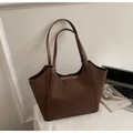 Braune Shopper-Tasche aus Leder mit Reißverschluss und Büro-Zubehör auf weißem Tisch - Braun