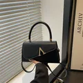 Elegant black shoulder bag with gold V-shaped metal buckle and asymmetric flap design - Black