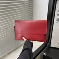 Elegante rode leren envelop clutch tas vastgehouden door model voor een stijlvolle achtergrond - Bordeauxrood