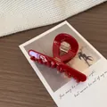 Elegante pinza per capelli in acetato rosso con logo dorato su sfondo in tessuto - Pinza Incrociata Rossa