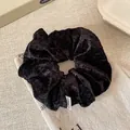 Minimalist black plush velvet scrunchie with soft chenille texture and elegant white label - Black