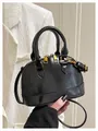 Detail of glossy black shell bag with gold zippers against a white blazer backdrop - Black