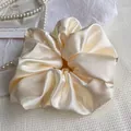 Elegant cream satin scrunchie with glossy pleated texture and small black woven label - Off White