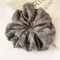 Elegant grey lace scrunchie with floral embroidery and brand label on a book - Scrunchie Style / Gray