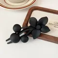 Matte black floral hair clip with five-petal flower and bead accents on wooden background - Black Flower Clip
