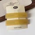 Set of two amber acetate rectangular hair clips on a minimalist beige card holder - Yellow