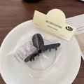Minimalist black acetate shark hair claw clip in elegant retail packaging on a plate - Black Cross Claw Clip