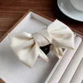 Elegant cream satin bow shark hair claw clip displayed on a velvet jewelry tray - Off White