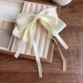 Cream white satin bow hair clip with long ribbons on a velvet jewelry display tray - Off White