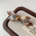 Chic acetate bow hair clip with amber marble texture on a rustic wooden display tray - Mixed Pattern