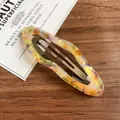 Colorful oval acetic acid hair clip with vibrant marble pattern on a wooden background - Tangerine Cloud Snap Clip